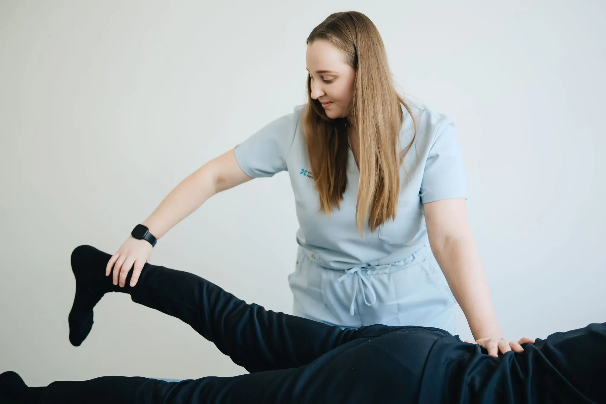 Physiothérapeute qui étire la jambe d'un patient allongé sur une table de traitement